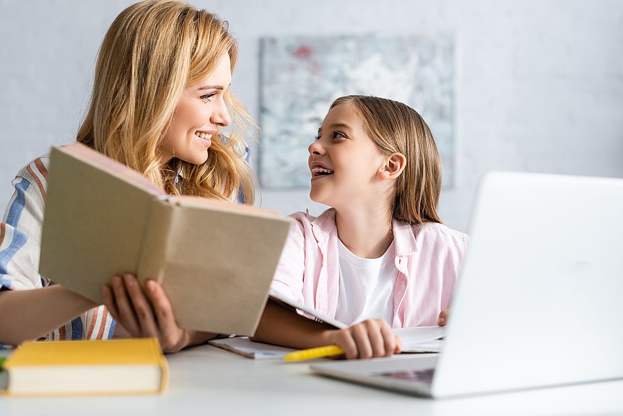 Selective focus of cheerful child looking at mother with book near laptop at table Foto: COLOURBOX
